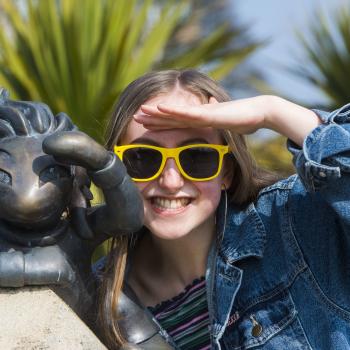 A girl wearing yellow sunglasses is copying a pose of a Lemmings statue